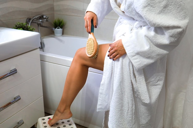 Foto una joven realiza un masaje con un cepillo de madera con cerdas naturales en casa en el baño t ...