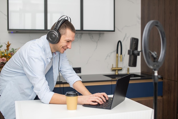 Un joven realiza una transmisión de video por teléfono Trabaja en una computadora portátil con auriculares