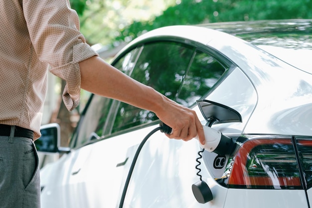 Foto un joven recarga la batería de un coche eléctrico desde una estación de carga