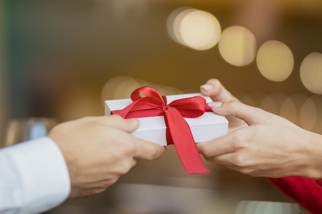 Una joven recibe un regalo de su novio. Fondo borroso cálido y encantador de un restaurante. Dos copas de vino y una rosa en la mesa del café. Concepto de San Valentín.