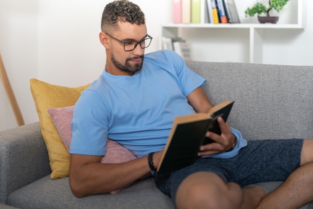 Joven recostado en el sofá leyendo un libro