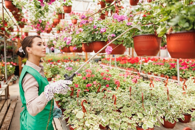 Una joven regando flores y cuidándolas en un centro de jardinería o en un vivero de plantas.