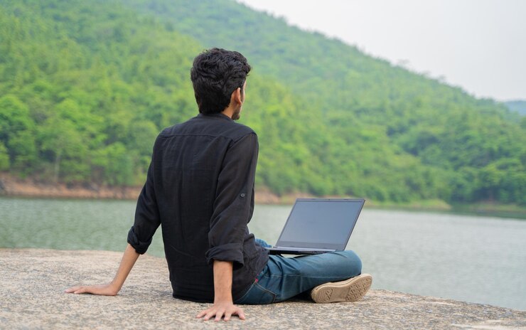Joven relajado trabajando en una computadora portátil y sentado en la naturaleza Concepto de trabajo y nómada digital