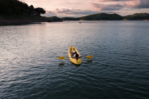 Joven relajándose en canoa amarilla con remo en el lago por la noche
