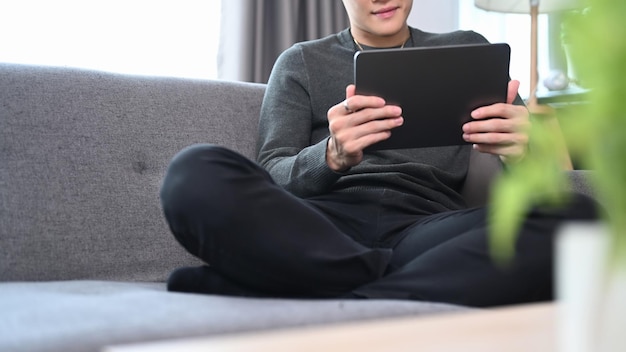 Joven relajándose en un cómodo sofá y usando tableta digital.