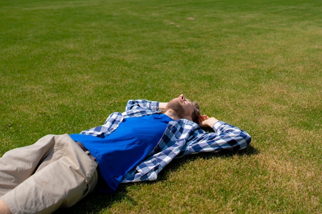 Joven relajarse al aire libre en el césped de hierba verde bajo los rayos del sol de verano