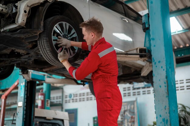 Joven reparador caucásico analizando y arreglando un auto roto en un taller mecánico de reparación de autos