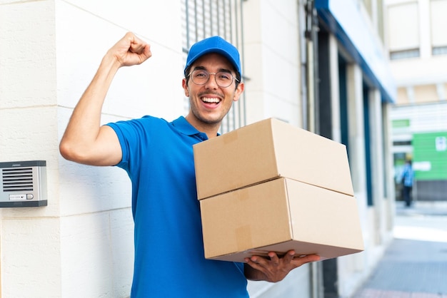 Joven repartidor al aire libre sosteniendo cajas y celebrando una victoria