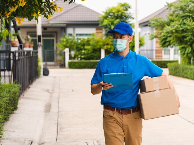 El joven repartidor asiático sostiene buzones de paquetes en el servicio de mascarillas protectoras y camina buscando la ubicación del hogar del cliente, bajo el toque de queda coronavirus pandémico COVID-19