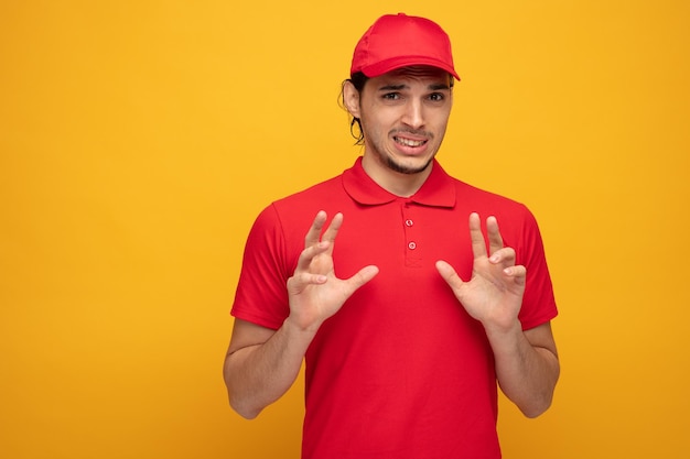 joven repartidor irritado con uniforme y gorra mirando a la cámara sin mostrar ningún gesto aislado en el fondo amarillo