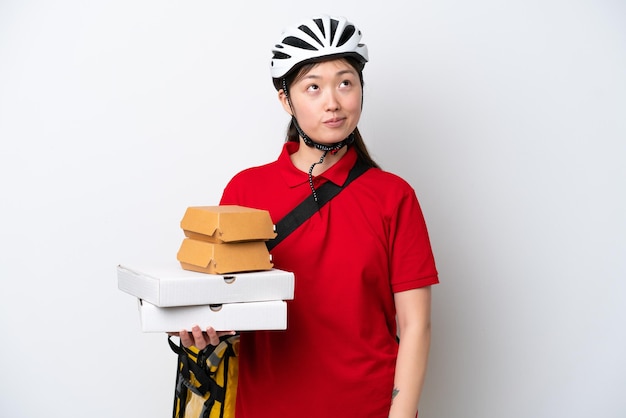 Joven repartidora china tomando comida para llevar aislada de fondo blanco y mirando hacia arriba