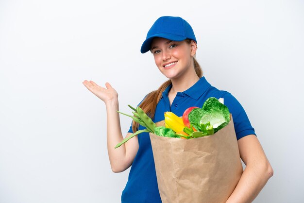 Joven repartidora tomando una bolsa de comida para llevar aislada de fondo blanco extendiendo las manos hacia un lado para invitar a venir