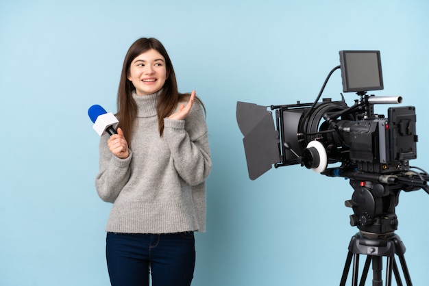 Joven reportero mujer sosteniendo un micrófono y reportando noticias riendo