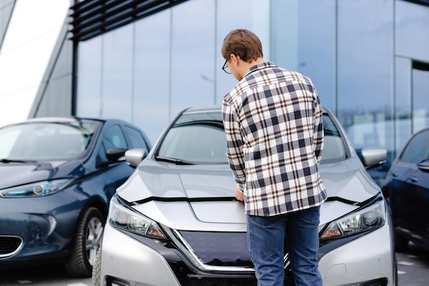 Joven revisando debajo del capó de su auto para averiguar cuál es el problema
