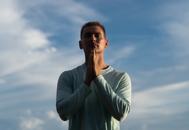 Joven reza sobre fondo de cielo azul. Concepto de arrepentimiento, arrepentimiento y esperanza.