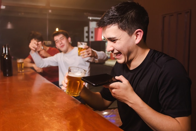 Un joven riendo mientras envía un audio de voz junto con sus amigos borrachos en el bar.