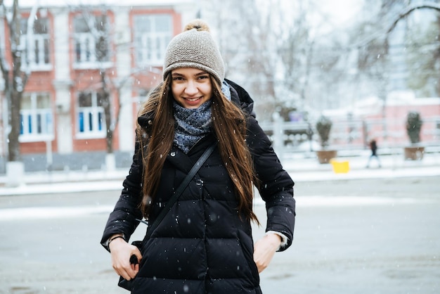 Una joven riendo con el pelo largo camina por las calles de la ciudad en invierno hace frío