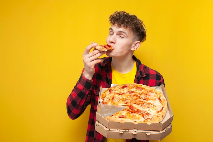 Foto un joven rizado comiendo pizza sobre un fondo amarillo. un estudiante hambriento disfrutando de comida rápida.