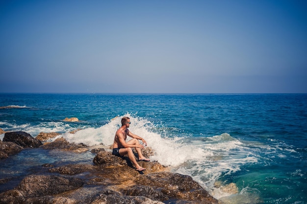 Un joven se para en las rocas con vistas al mar Mediterráneo abierto Un chico en un cálido día soleado de verano mira la brisa del mar