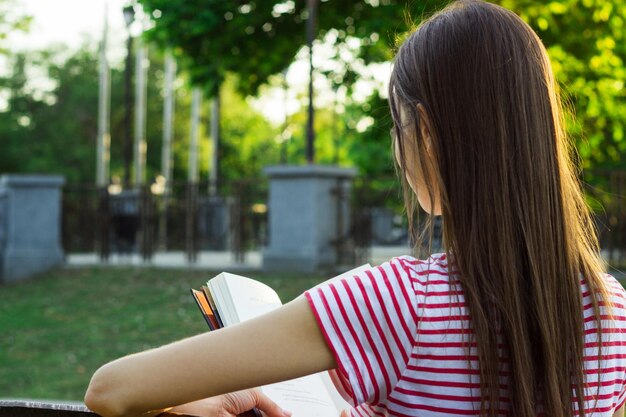 Una joven romántica leyendo un libro en el parque en un día soleado de verano. Vista trasera.