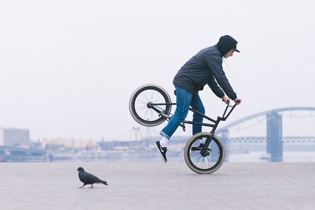 Un joven en ropa casual monta en una rueda delantera de bicicleta bmx. Trucos en bmx