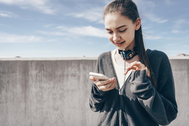 Una joven con ropa deportiva elegante se fortalece antes de entrenar al aire libre mira su teléfono inteligente