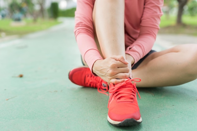 Foto una joven con ropa deportiva rosa se lastimó el tobillo durante el ejercicio en el parque sección baja de una chica deportiva que sufre de un tobillo volteado mientras estaba sentada en la pista durante un accidente por concepto de ejercicio