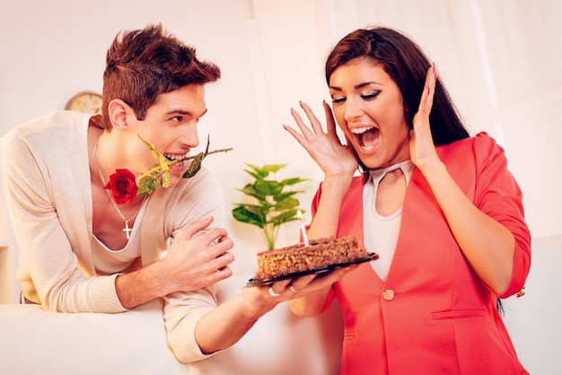 Un joven con una rosa en la boca le da pastel de cumpleaños a la hermosa chica.