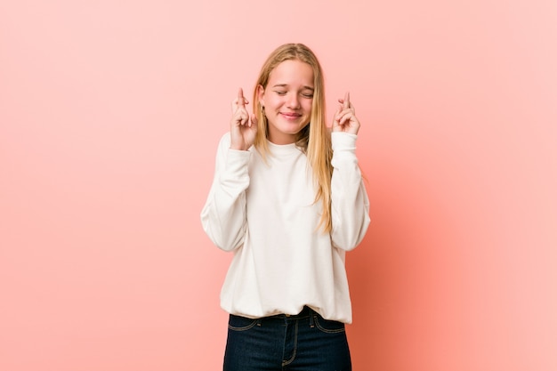 Joven rubia adolescente mujer cruzando los dedos para tener suerte