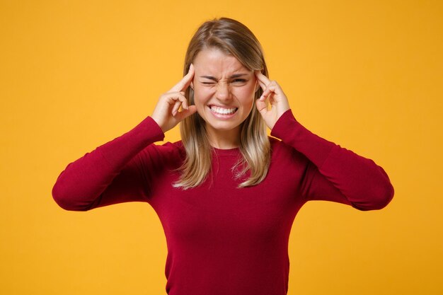 Una joven rubia agotada con ropa informal posando aislada en un retrato de estudio de fondo naranja amarillo. Concepto de estilo de vida de las personas. Simulacros de espacio de copia. Ponerse la mano en la cabeza, tener dolor de cabeza.