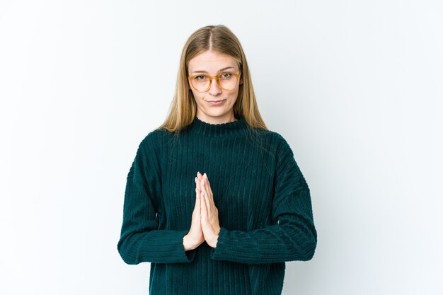 Joven rubia aislada en blanco rezando, mostrando devoción, persona religiosa en busca de inspiración divina.