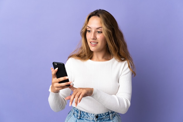 Joven rubia aislada en morado enviando un mensaje o correo electrónico con el móvil