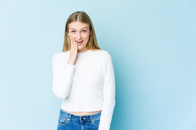 Joven rubia aislada en la pared azul grita fuerte, mantiene los ojos abiertos y las manos tensas.