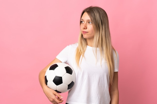 Joven rubia aislada en rosa con balón de fútbol