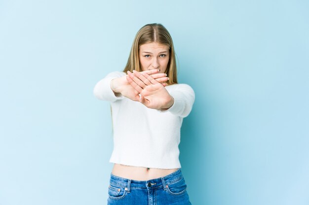 Joven rubia aislada sobre fondo azul de pie con la mano extendida mostrando la señal de stop, impidiéndote.