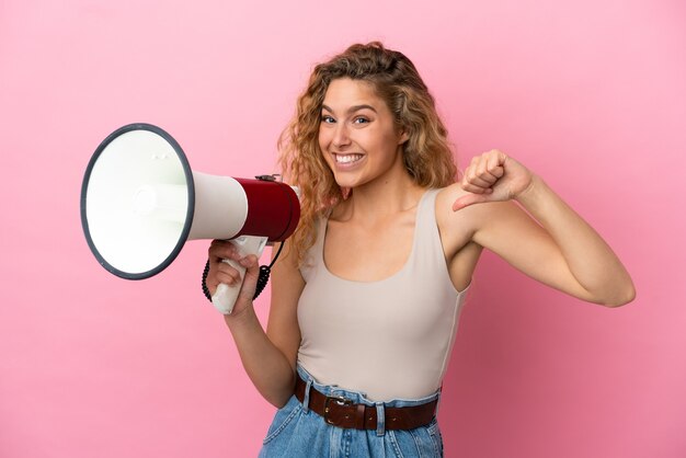 Joven rubia aislada sobre fondo rosa sosteniendo un megáfono y orgullosa y satisfecha de sí misma