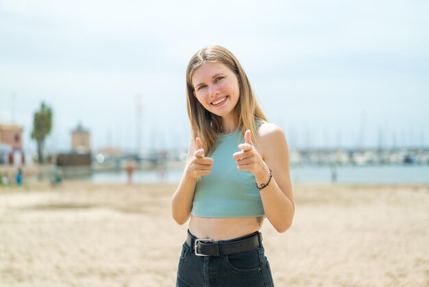 Joven rubia al aire libre apuntando al frente y sonriendo