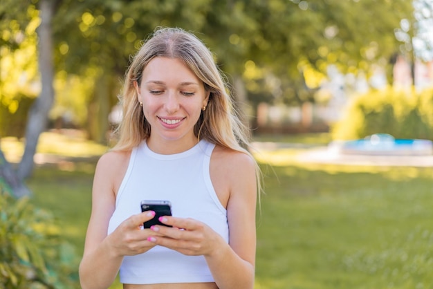 Joven rubia al aire libre enviando un mensaje con el móvil