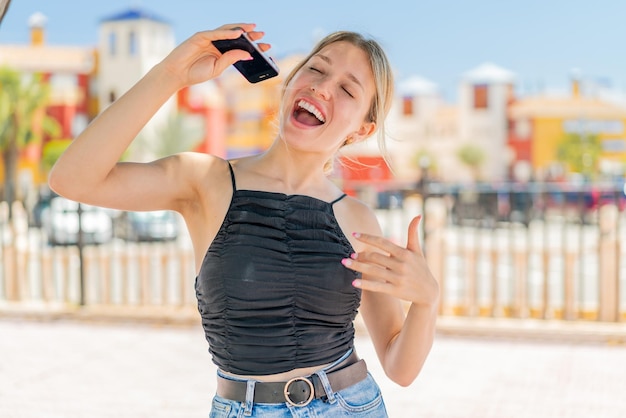 Joven rubia al aire libre usando teléfono móvil y cantando