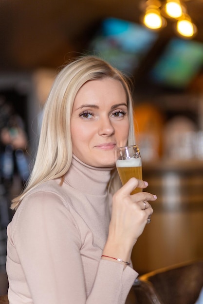 Una joven rubia alegre te mira mientras brinda con un vaso de cerveza.