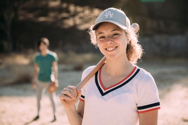 Joven rubia con bate de béisbol contra el fondo de la naturaleza y el hombre con guante