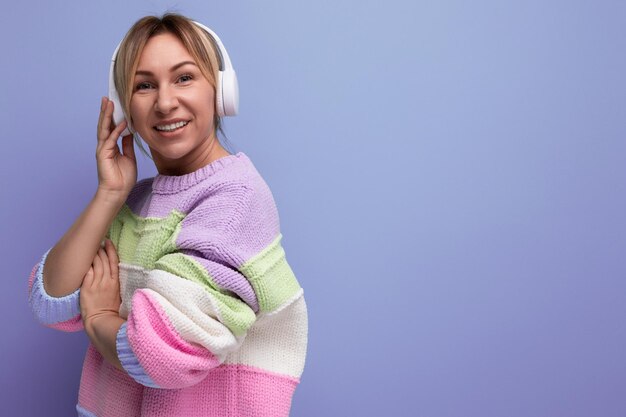 Joven rubia brillante escucha música en grandes auriculares blancos sobre un fondo morado con copia