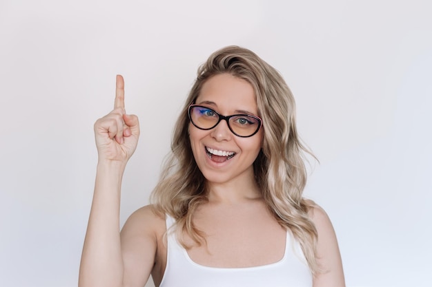 Una joven rubia con cabello ondulado en gafas gesticulando con la mano haciendo el dedo hacia arriba