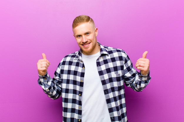 Joven rubia con camisa cuadrada sonriendo alegremente y luciendo feliz, sintiéndose despreocupado y positivo con ambos pulgares arriba