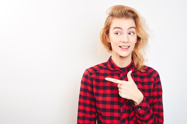 Una joven rubia con camisa roja apuntando con su dedo en el fondo