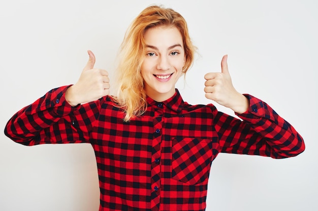 Una joven rubia con camisa roja mostrando los pulgares para arriba