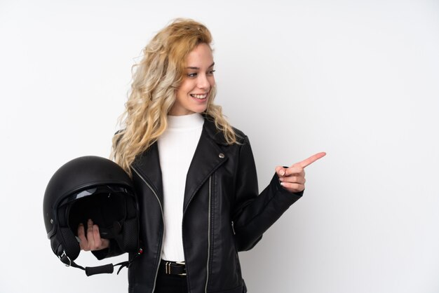 Joven rubia con un casco de moto aislado en la pared blanca apuntando hacia un lado para presentar un producto