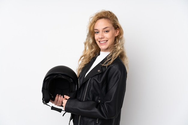 Joven rubia con un casco de moto aislado en la pared blanca sonriendo mucho