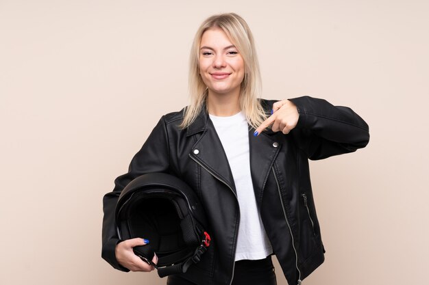 Joven rubia con un casco de moto sobre pared aislada y apuntando