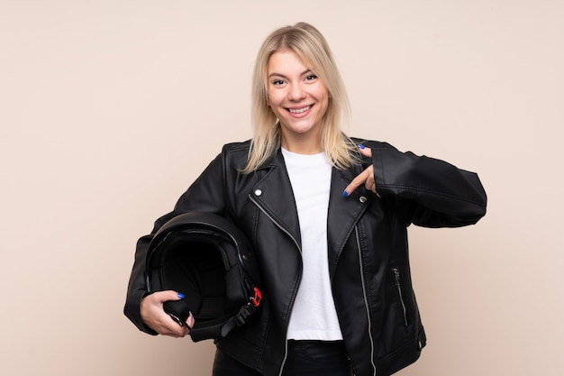 Joven rubia con un casco de moto sobre pared aislada con expresión facial sorpresa